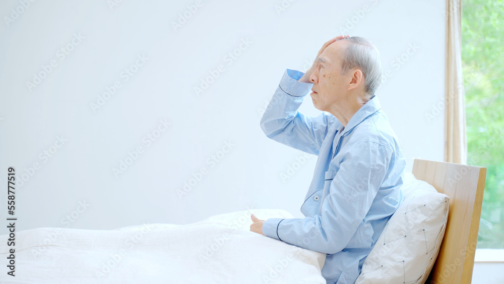 ベッドで頭を押さえる高齢者 ベッドで頭を押さえる高齢者