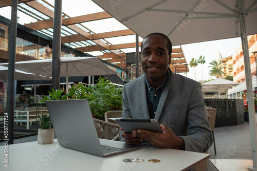 Wallpaper Mural Young African trader monitors the market with laptop and tablet; the subject smiles at the camera. Torontodigital.ca