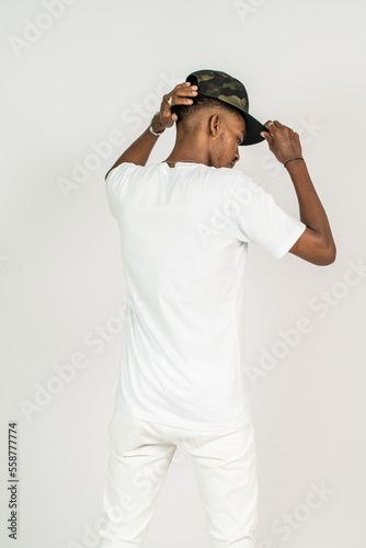 Back side of an african man wearing white blank shirt, doing a pose with both of his hand on his hat
