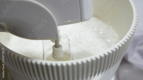 The woman chef whips the ingredients for baking with a mixer. Whipped cream with a mixer, whisk for whipping.