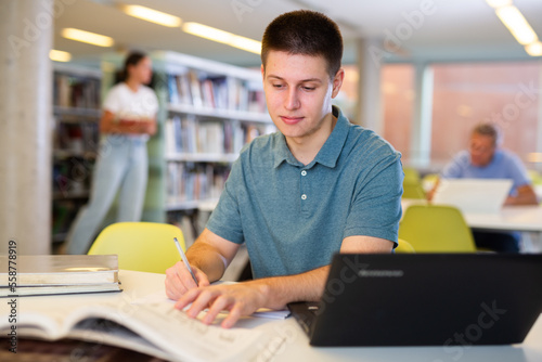 Positive young man in casual clothes working remotely using a computer in a quiet library