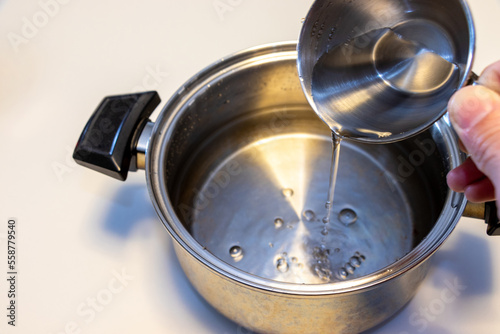 カップで量を量りながら鍋に水を入れる 