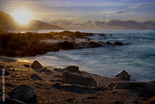 Long exposure landscape of the sunset on the beach. Seasape of waves breaking on the rocks of the Galician coast. Sunstar over the mountain. Baiona, Rias Baixas, Galicia, Spain