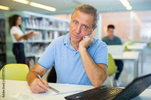 View on a bored mature man with a laptop in the library. High quality photo photo