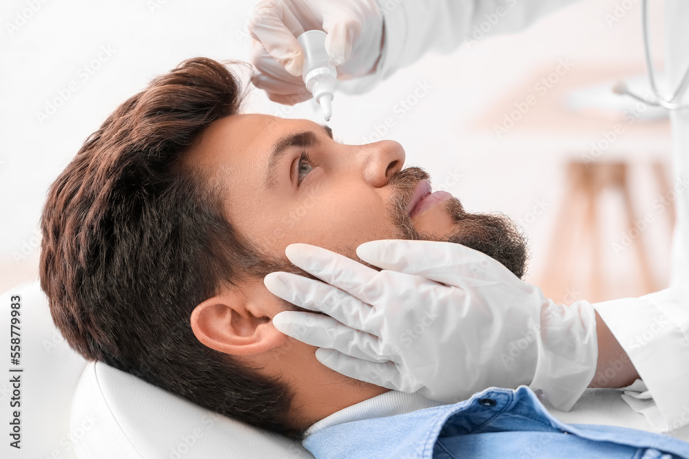 Ophthalmologist putting drops in young man's eye at hospital, closeup