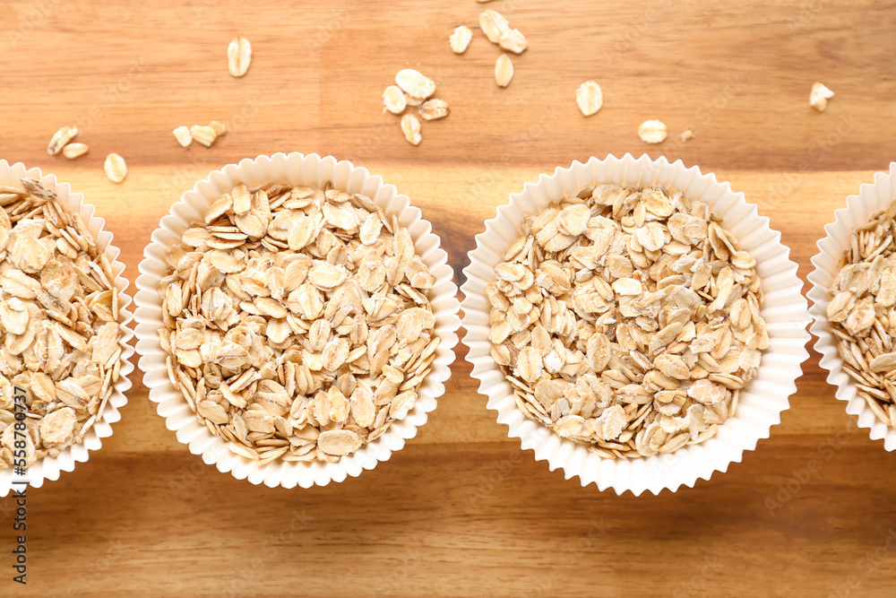 Wooden board with paper baking cups of raw oatmeal, closeup Wooden board with paper baking cups of raw oatmeal, closeup