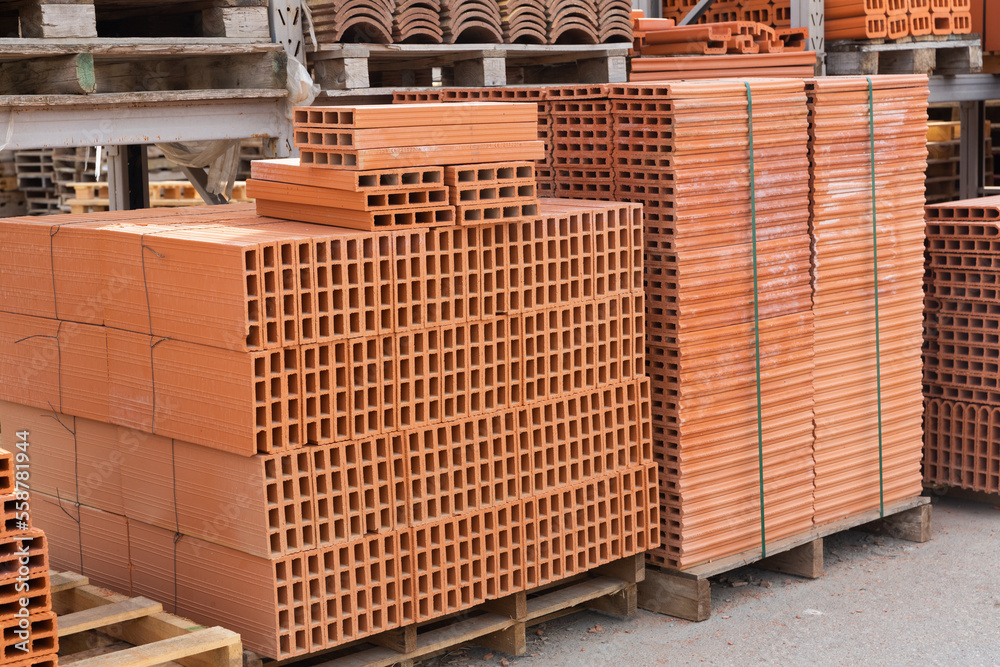 Red brick packed in stacks are stored on ground outdoors at a hardware ...