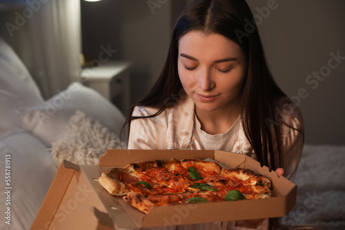 Young woman with box of tasty pizza in bedroom at night, closeup