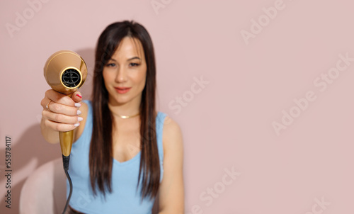 Young brunette woman with long hair holding hair dryer. Hair care concept. Banner with copy space for a hairdresser. (ID: 558784117)