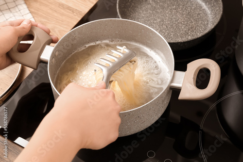 Woman preparing delicious pasta on electric stove in kitchen