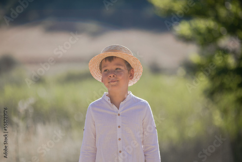 Portrait of the blode hair boy in straw hat with blurred summer greenery background