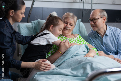 Tela Happy little girl greeting sick grandmother with hug on hospital room visit