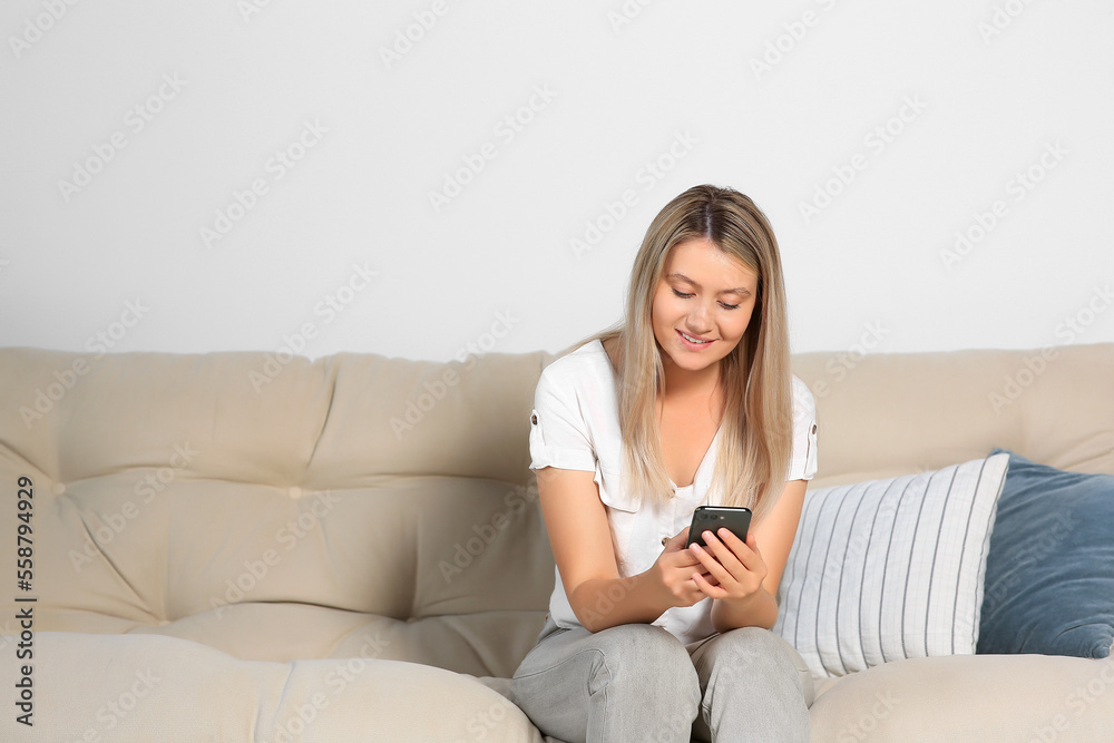 Woman using smartphone on sofa at home. Space for text
