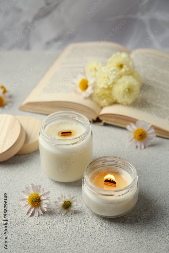 Burning scented candles and chamomile flowers on light gray textured table