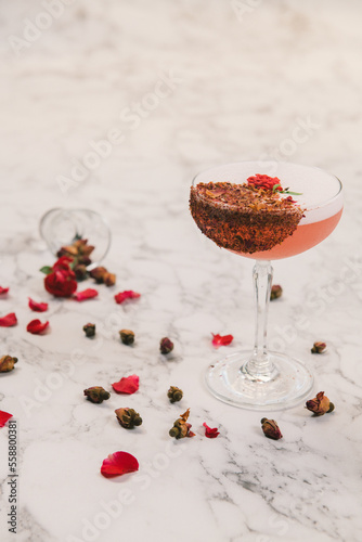 A sweet pink sparkling beverage decorated with crusted chocolate and small roses in a coupe glass.