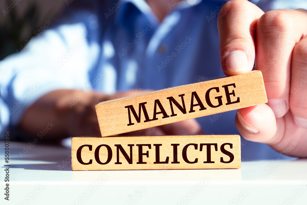 Closeup on businessman holding a wooden block with MANAGE CONFLICTS message, business concept Closeup on businessman holding a wooden block with MANAGE CONFLICTS message, business concept