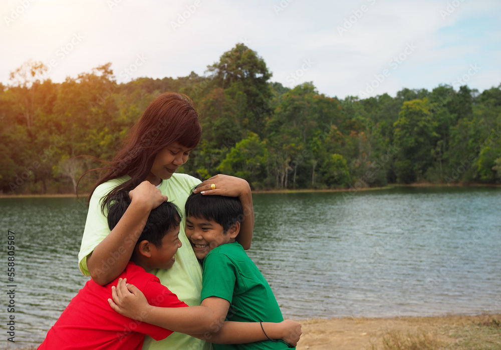 Happy family spending time outdoors hugging and enjoying the view of river. Mother with two kids.