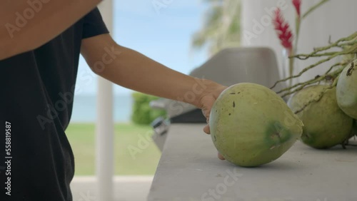 Middle shot of a man cutting a coconut with big knife, on the table near outdoorsman grill, outdoors on the open kitchen