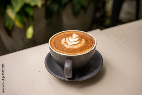 Cup of art latte on a cappuccino coffee isolated on green garden blurry  background