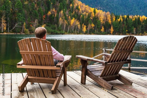 Man resting in Comfortable wooden sun lounger Adirondack, Westport against of colorful mountains with emerald lake