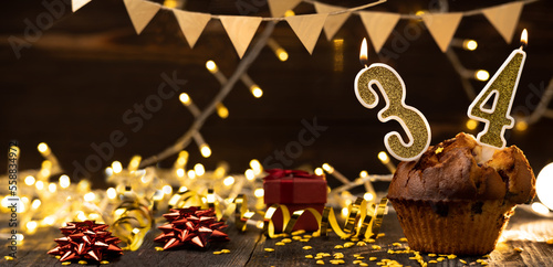 Number 34 birthday celebration candle in cupcake against lights and wooden background. photo