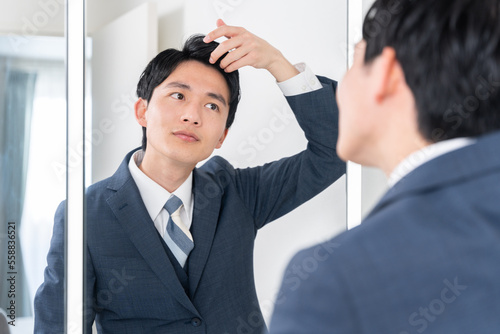 洗面所で鏡を見てヘアセットする若いビジネスマン（髪の毛・朝・出勤準備）