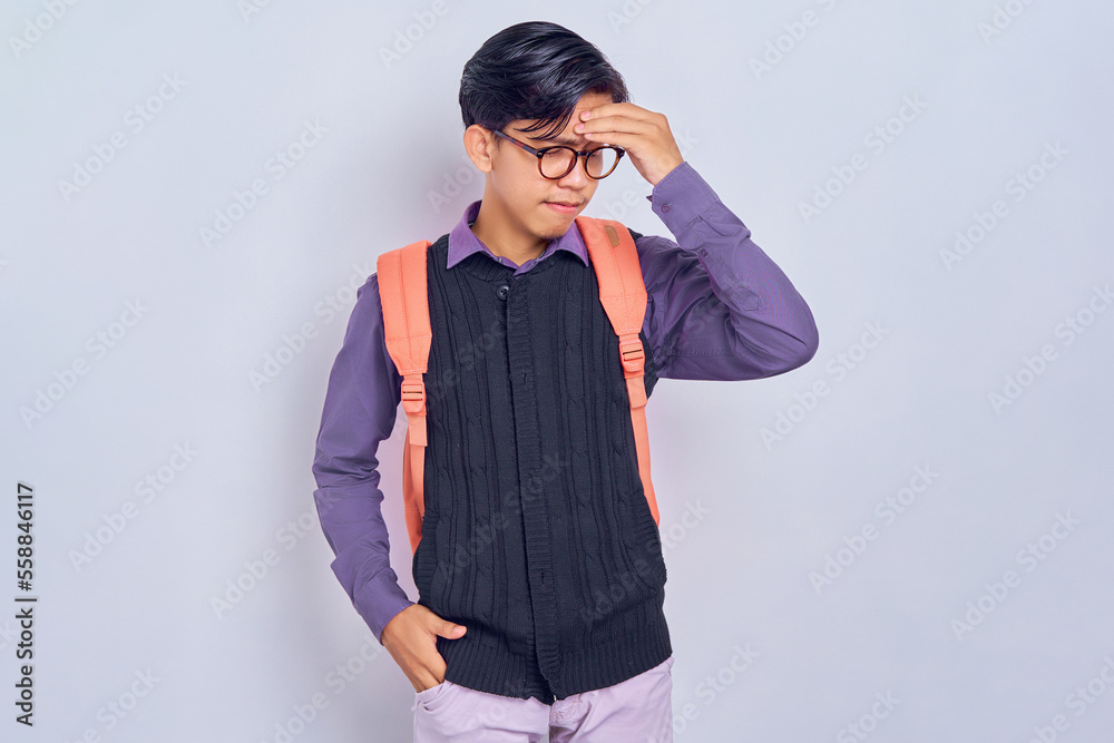 tired young Asian student man in casual clothes with backpack Keeping his eyes closed, put hand on head isolated on gray background. High school university college concept tired young Asian student man in casual clothes with backpack Keeping his eyes closed, put hand on head isolated on gray background. High school university college concept