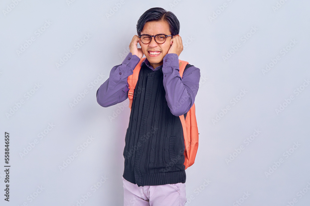 Displeased young Asian student man in casual clothes with backpack Covering ears with hand isolated on gray background. High school university college concept Displeased young Asian student man in casual clothes with backpack Covering ears with hand isolated on gray background. High school university college concept