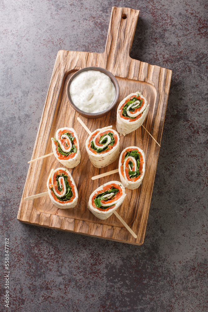 Norwegian roll of smoked salmon, cream cheese and herbs wrapped in flat bread close-up on a wooden board on the table. Vertical top view from above