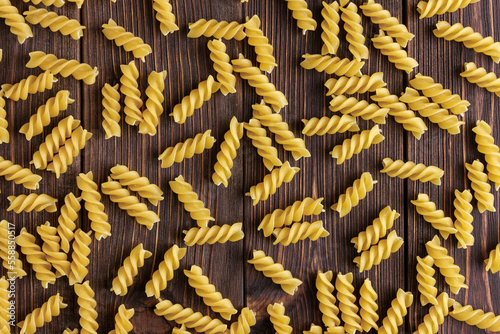Raw pasta fusilli texture on wooden background.