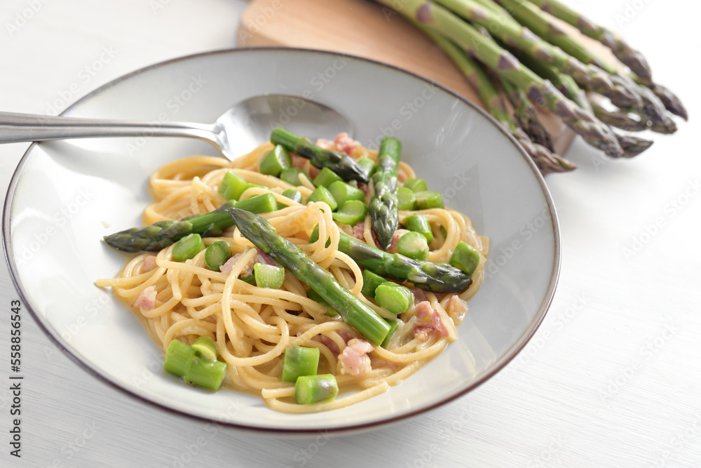 Spaghetti with green asparagus, bacon and egg as carbonara sauce variation on a plate and on a white painted wooden table, selected focus Spaghetti with green asparagus, bacon and egg as carbonara sauce variation on a plate and on a white painted wooden table, selected focus