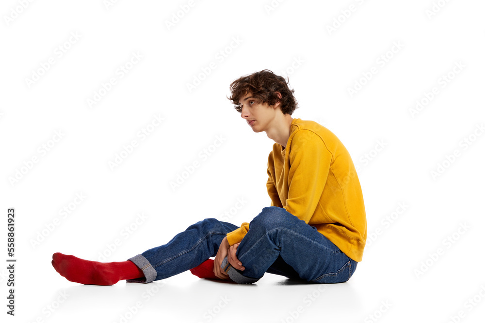 Portrait of young boy sitting on floor in sadness, feeling asocial over white background. Loneliness, depression Portrait of young boy sitting on floor in sadness, feeling asocial over white background. Loneliness, depression
