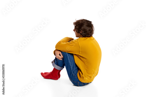 Portrait of young boy sitting on floor in depression, hugging legs over white background. Feeling lonely, sad. Introvert © master1305