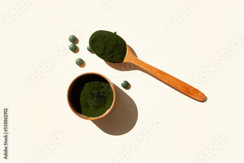 Spirulina powder in a wooden spoon on a white background with contrast shadows. Flat style.