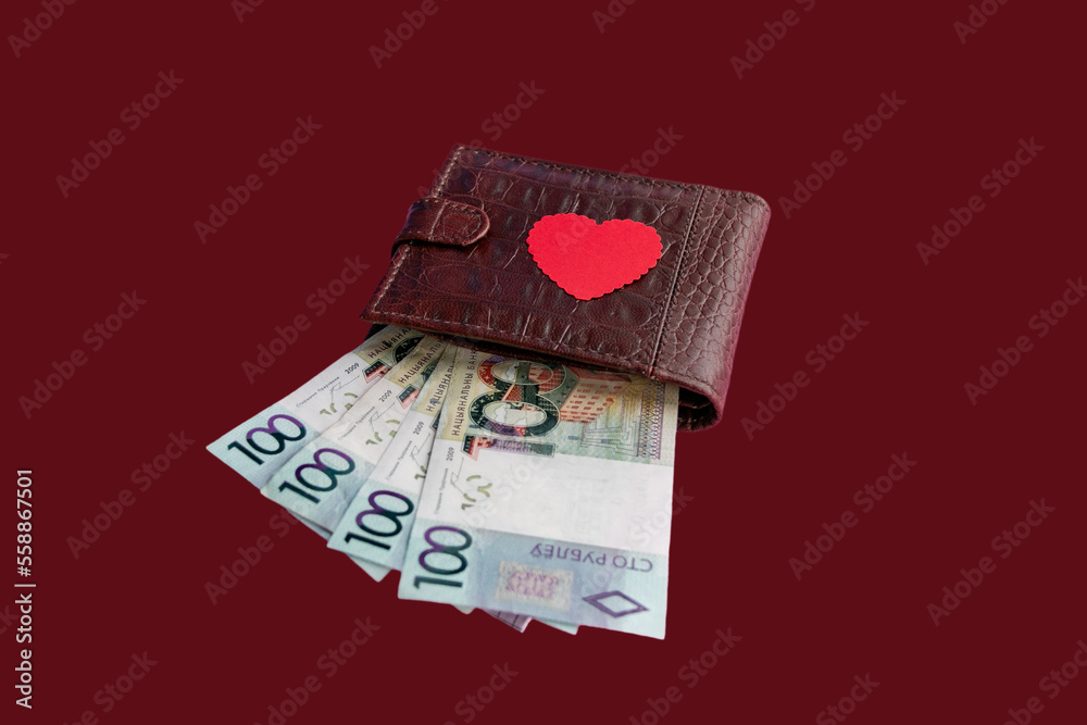 Brown leather wallet with red heart. Belarusian hundred-ruble bills stick out of the wallet. The concept of cash costs for the purchase of gifts for Valentine's Day, wedding, birthday. Close-up.