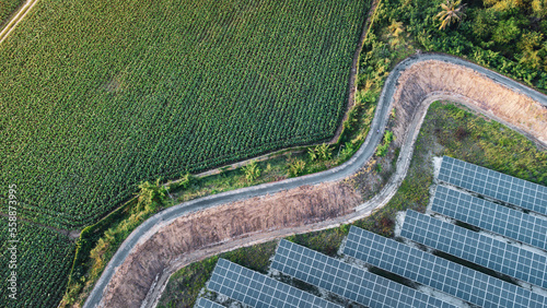 Fly over Solar cells farm beside nature green farm around large industrial factory area. Solar farms are generating renewable energy for the industry.