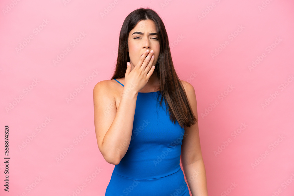 Young Brazilian woman isolated on pink background yawning and covering wide open mouth with hand