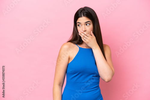 Young Brazilian woman isolated on pink background doing surprise gesture while looking to the side