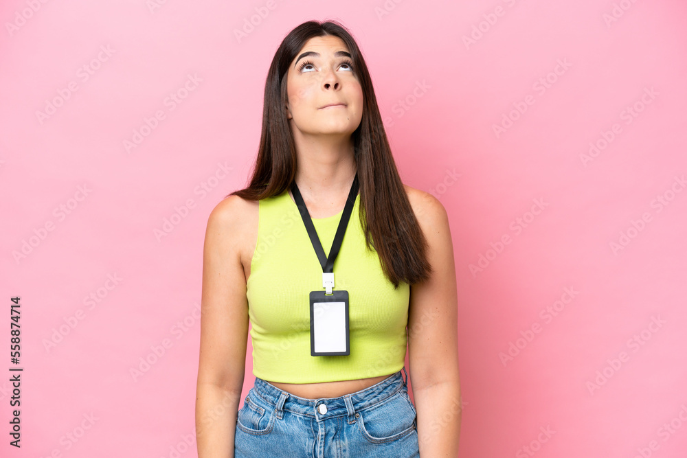 Young Brazilian woman with ID card isolated on pink background and looking up Young Brazilian woman with ID card isolated on pink background and looking up