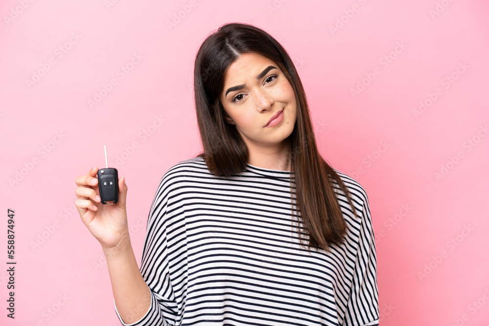 Young Brazilian woman holding car keys isolated on pink background with sad expression Young Brazilian woman holding car keys isolated on pink background with sad expression