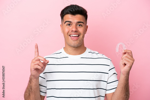 Young caucasian man holding invisaling isolated on pink background pointing up a great idea photo