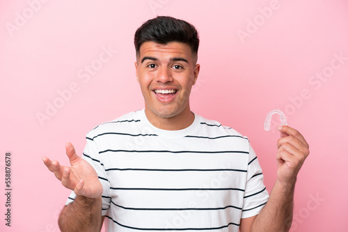 Young caucasian man holding invisaling isolated on pink background with shocked facial expression photo