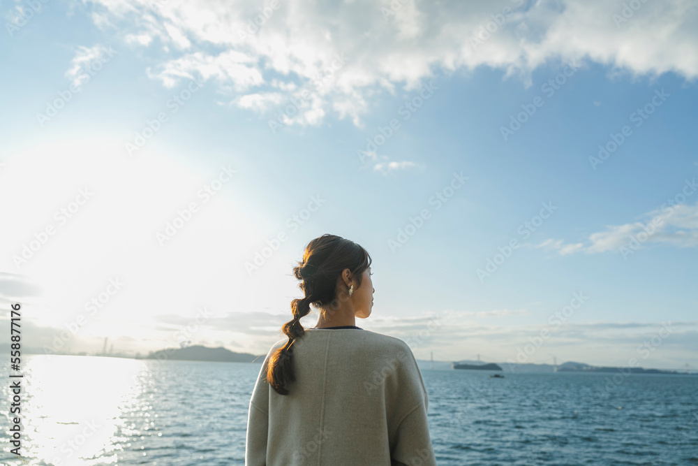 冬の海で夕日を見ている女性