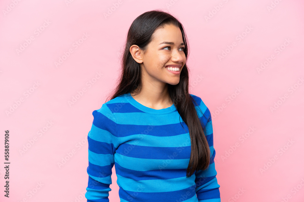Fototapeta premium Young Colombian woman isolated on pink background looking to the side and smiling