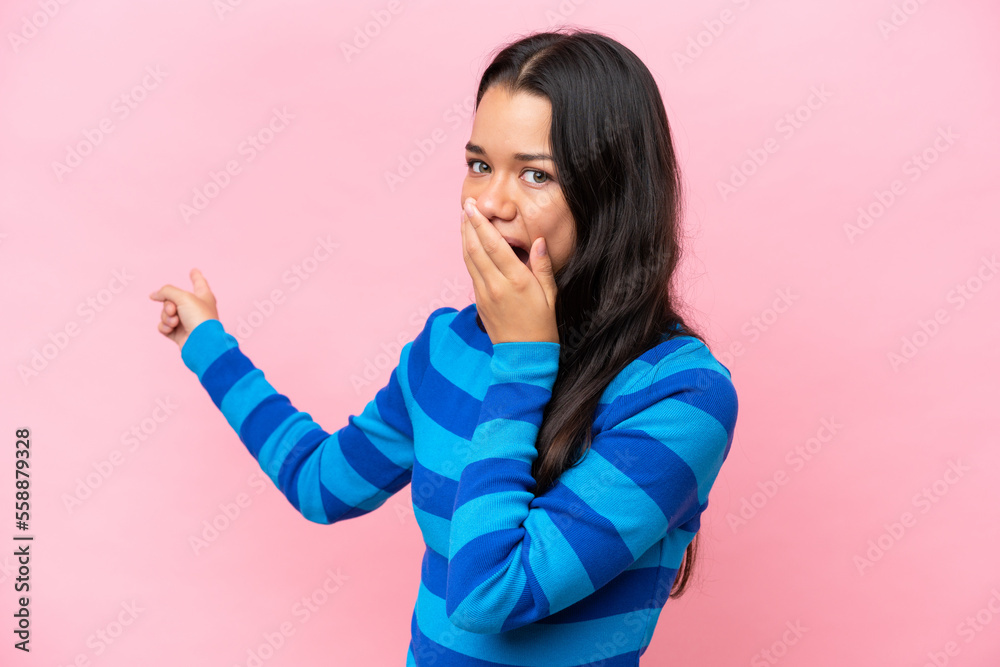 Young Colombian woman isolated on pink background with surprise expression while pointing side Young Colombian woman isolated on pink background with surprise expression while pointing side