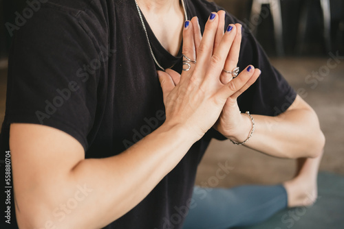 Side close-up photo of torso and hands of a female yogi new teacher in skandasana pose with hands to heart wearing green leggings in her yoga practice on a mat on the floor © Sandra