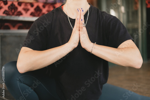 Close-up photo of the torso of a woman yogi in a skandasana or side lunge pose with hands to heart wearing green leggings in her yoga practice on a mat on the floor photo