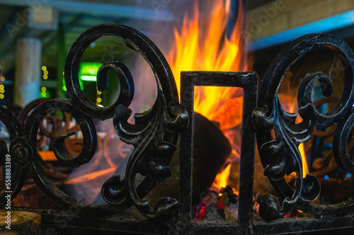 Fireplace for heating in a country house in winter. Metal wrought-iron fireplace railing. The red color of the flame when gorenje wood in the fireplace. photo