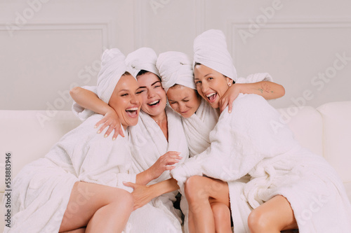 A group of women spend leisure time. Young attractive females in bathrobes chat merrily.