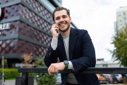 young businessman talking on a mobile phone against the background of a modern office building with a smile on his face